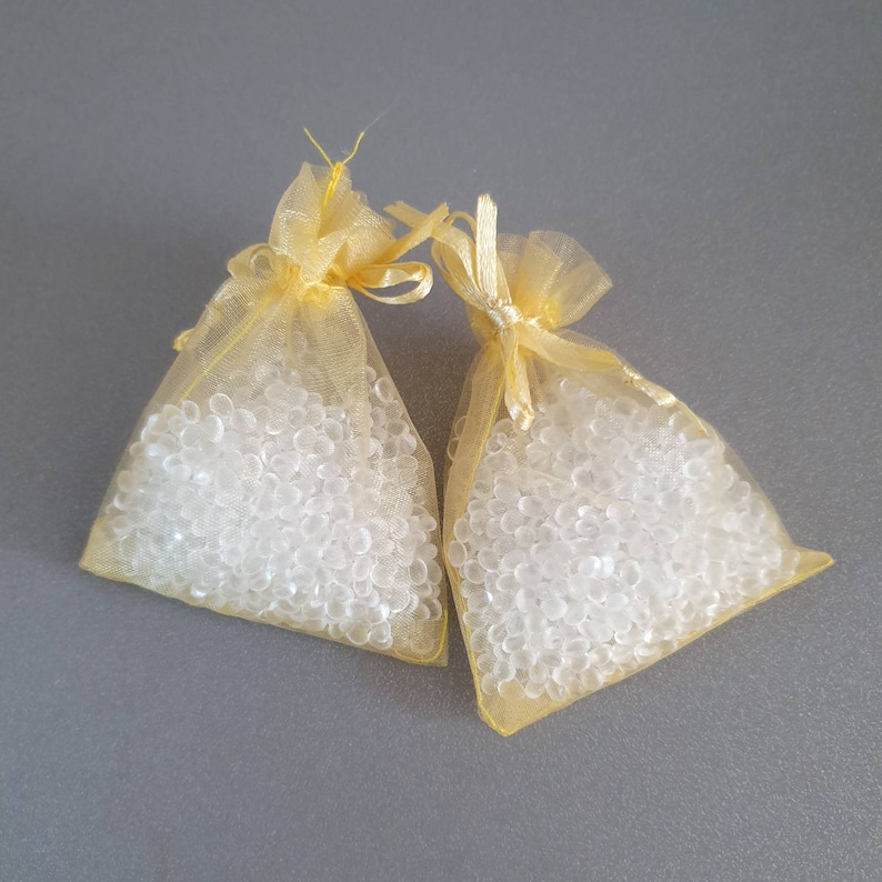 May include: Two small yellow mesh bags filled with clear silica gel beads. The bags are tied with a ribbon.