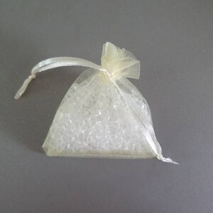 May include: A small, ivory-colored mesh bag filled with clear, round beads. The bag has a drawstring closure and is tied with a white ribbon.