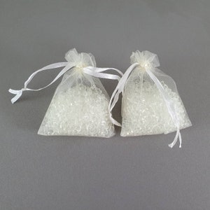 May include: Two white organza bags filled with clear silica gel beads. The bags have white ribbon ties.