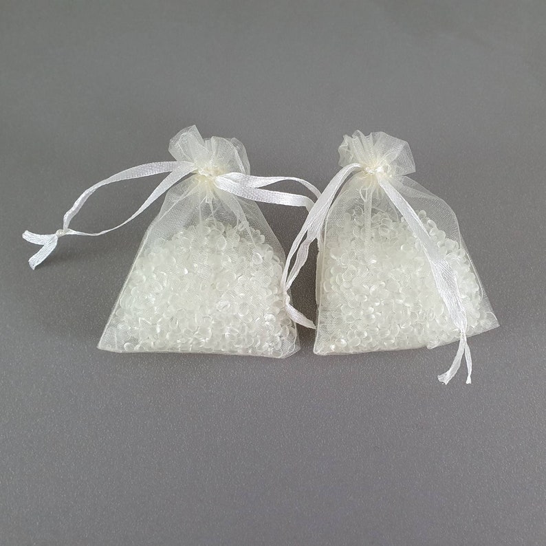 May include: Two white organza bags filled with clear silica gel beads. The bags have white ribbon ties.