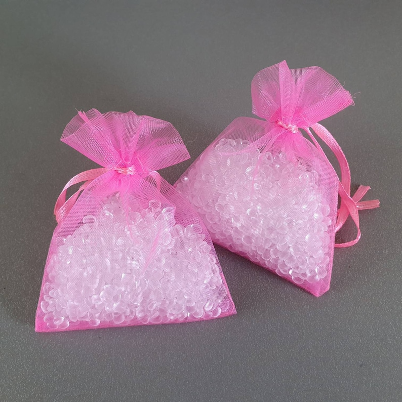 May include: Two pink tulle bags filled with clear, round beads. The bags are tied with a pink ribbon.