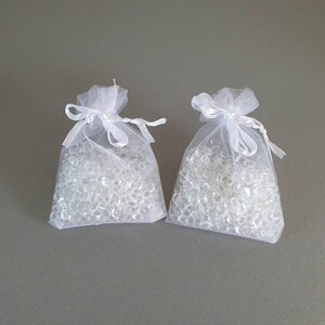 May include: Two white organza bags filled with clear silica gel beads. The bags are tied with white ribbon.