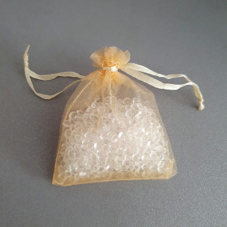 May include: A small, clear, plastic bag filled with clear, round beads. The bag is made of a sheer, light gold material and has a drawstring closure.