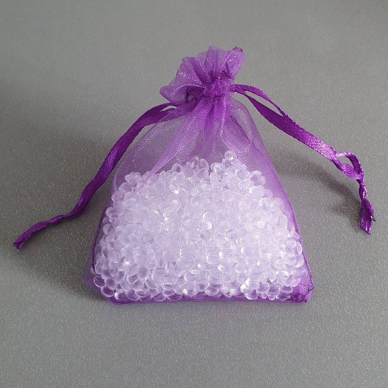 May include: A purple organza drawstring bag filled with clear, small, round, plastic beads.