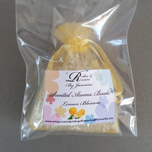 May include: A small yellow organza bag filled with white scented aroma beads. The bag has a label that reads "Relax & Revive By Jasmine Scented Aroma Beads Lemon Blossom" and a website address.