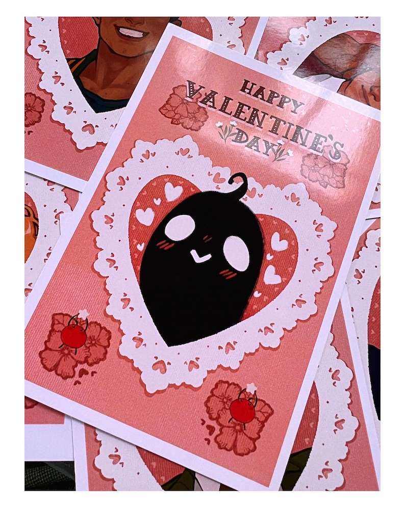 Puede incluir: Tarjeta de felicitaci&oacute;n del D&iacute;a de San Valent&iacute;n con fondo rosa y un personaje de dibujos animados negro dentro de un marco en forma de coraz&oacute;n. La tarjeta presenta el texto "Happy Valentine's Day" en una fuente decorativa, con motivos florales y de coraz&oacute;n.
