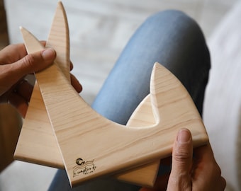 May include: Two wooden pieces of a guitar stand, made of light wood, with a logo that says "Le Capitaine de Toulon" on the bottom piece.
