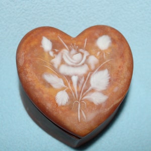 May include: A heart-shaped box made of light brown alabaster with a white carved rose design.
