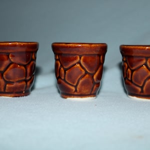May include: Three small brown ceramic pots with a textured stone-like design. The pots are all the same size and shape.