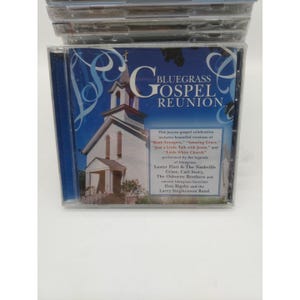 Pode incluir: Uma caixa de CD com o álbum "Bluegrass Gospel Reunion". A capa mostra uma igreja branca contra um fundo azul. O texto inclui o título do álbum e nomes de artistas, como Lester Flatt & The Nashville Grass.