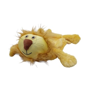 Puede incluir: Un león de peluche amarillo y beige. El león tiene una cabeza redonda con una nariz marrón, ojos negros y una boca sonriente. Tiene una melena peluda y patas extendidas.
