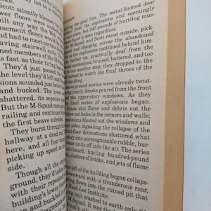 Peut inclure: Pages d'un livre ouvert avec du texte imprim&eacute;. Le texte d&eacute;crit une sc&egrave;ne avec des explosions, une escouade et un b&acirc;timent en effondrement. Les pages sont jaunies, sugg&eacute;rant l'&acirc;ge. Le livre est ouvert, r&eacute;v&eacute;lant le texte.