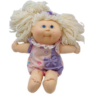 May include: A Cabbage Patch Kids doll with light skin, blue eyes, and thick, wavy blonde yarn hair. The doll wears a sleeveless romper featuring a light pink section with colorful floral and letter patterns, a solid purple section, and a small bow.