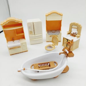 Puede incluir: Un conjunto de muebles de casa de muñecas en miniatura que incluye una bañera blanca con rejilla dorada, un mueble de lavabo color crema, un frigorífico de dos puertas, una cocina con campana, un inodoro con tapa y un tocador con espejo.