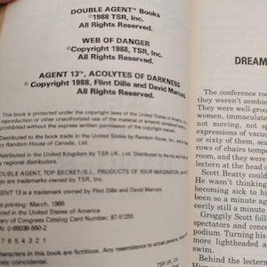 Peut inclure: Pages d'un livre ouvert avec du texte des livres "DOUBLE AGENT", dont "WEB OF DANGER" et "AGENT 13, ACOLYTES OF DARKNESS". Informations de copyright et num&eacute;ro de la Biblioth&egrave;que du Congr&egrave;s.