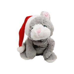 Può includere: Un peluche a forma di gatto grigio con muso bianco, naso rosa e baffi. Il gatto indossa un cappello da Babbo Natale rosso e bianco. Il giocattolo è progettato per stare seduto e ha una consistenza morbida e soffice, perfetto per le feste.