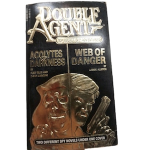 Peut inclure: Un livre de poche vintage intitul&eacute; "Double Agent" avec des lettres et des images dor&eacute;es en relief. La couverture pr&eacute;sente un cr&acirc;ne et un homme tenant une arme &agrave; feu, avec les titres "Acolytes of Darkness" et "Web of Danger". Le livre est une collection de romans d'espionnage.
