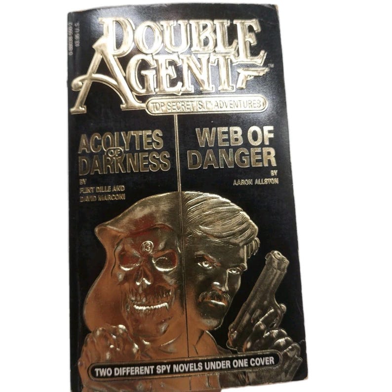 Peut inclure: Un livre de poche vintage intitul&eacute; "Double Agent" avec des lettres et des images dor&eacute;es en relief. La couverture pr&eacute;sente un cr&acirc;ne et un homme tenant une arme &agrave; feu, avec les titres "Acolytes of Darkness" et "Web of Danger". Le livre est une collection de romans d'espionnage.