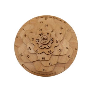 May include: A wooden puzzle with a circular design. The puzzle has multiple layers of wooden pieces with numbers and the text "REVOLVING CENTURY" and "ALIGN COLUMNS TO EQUAL ONE HUNDRED". The center piece has the number 100.