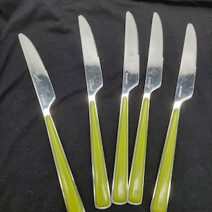 May include: Set of five stainless steel knives with bright green handles. The blades are silver and curved, with a serrated edge on one knife. The handles are a solid, glossy green color. The knives are arranged on a black surface.