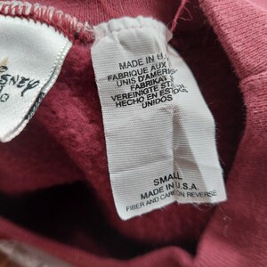 May include: Close-up of a red garment tag with multiple lines of text in English, French, German, and Spanish. The tag reads "MADE IN U.S.A." and "FIBER AND CARE ON REVERSE."