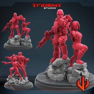 Pode incluir: Três figuras de ação pintadas de vermelho, dois homens e uma mulher, em pé em bases rochosas. As figuras seguram armas e estão em posição de combate. As figuras fazem parte de um conjunto e são projetadas para jogos de mesa.