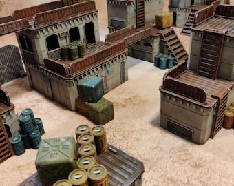 May include: A miniature, modular sci-fi terrain set featuring buildings, walkways, and containers. The structures are primarily gray with brown accents, ladders, and rooftops. Various containers and barrels are scattered throughout the scene, creating a detailed, post-apocalyptic environment.