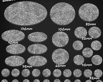 Può includere: Una collezione di basi grigie strutturate in varie dimensioni, tra cui forme ovali e circolari. Le dimensioni variano da 25 mm a 170 mm, con il testo "GOONMASTER". Le basi presentano un design a terra crepata.