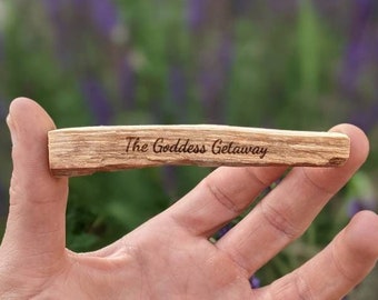 以下が含まれることがあります： 「The Goddess Getaway」と刻まれた木の棒。棒は人の手に持たれている。
