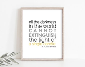 May include: A framed print with the quote "all the darkness in the world cannot extinguish the light of a single candle." The text is in black and yellow, with the author's name at the bottom. The frame is light brown.