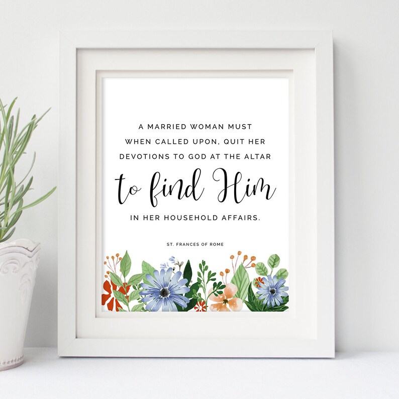 May include: A white framed print with a quote by St. Frances of Rome. The quote reads "A married woman must when called upon, quit her devotions to God at the altar to find Him in her household affairs." The print is decorated with a floral border of blue, orange, and green flowers.
