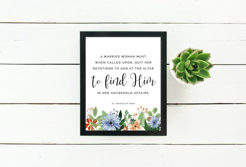 May include: A framed print with a white background and black frame. The print features a quote in black text that reads "A married woman must when called upon, quit her devotions to God at the altar to find Him in her household affairs." The quote is attributed to "St. Frances of Rome." The print is decorated with a floral border of blue, orange, and green flowers.