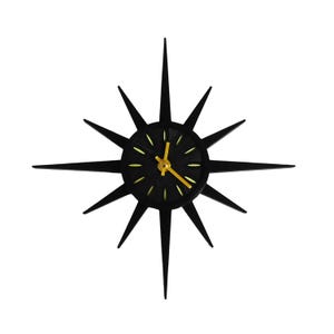 May include: A black starburst clock with a yellow clock face and hands. The clock has sharp, pointed rays extending outward from the center. The clock's hands point to 10:08.