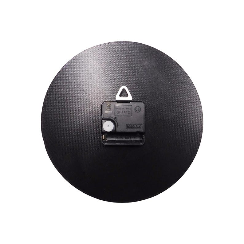 May include: A black, circular clock back with a textured finish. The quartz clock mechanism is visible, including the battery compartment and a metal hanger for wall mounting.