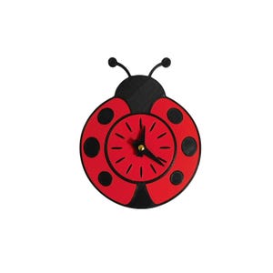 May include: A red and black ladybug-shaped wall clock. The clock face is red with black dots and black hands. The clock has a gold-colored center and black antennae.