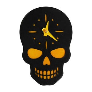 May include: A black skull-shaped wall clock with yellow accents. The clock features yellow eyes, nose, and teeth, with a yellow clock hand. The clock is a decorative item.