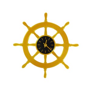 May include: A gold-colored ship's wheel clock with a black clock face. The clock hands are gold, and the wheel has eight spokes. The clock is a nautical-themed decorative item.