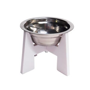 May include: A stainless steel bowl with a polished silver finish, set into a white, elevated, four-legged stand. The bowl features a wide, flat rim that rests securely on the top of the white support structure, creating a raised feeding station.