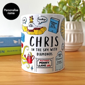 Puede incluir: Taza de cerámica blanca con un diseño colorido que presenta un submarino amarillo, el nombre "Chris" y la frase "In the Sky with Diamonds". La taza incluye ilustraciones de un libro, una regadera roja y una señal de tráfico.