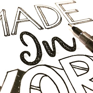 Puede incluir: Primer plano de una superficie blanca con las palabras "MADE IN" en letras negras dibujadas a mano. Un bol&iacute;grafo negro est&aacute; en la esquina superior derecha. La palabra "MADE" est&aacute; en estilo 3D.