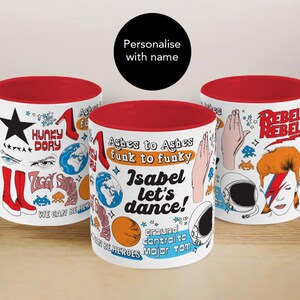 Puede incluir: Tres tazas de cerámica blancas con interiores y asas rojas. Cada taza presenta ilustraciones coloridas y texto, incluyendo estrellas, zapatos y las palabras "HUNKY DORY", "Ashes to Ashes" y "Rebel Rebel". Las tazas están decoradas con varios gráficos.