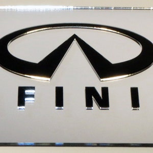 May include: A silver metal license plate frame with the Infiniti logo and the word "INFINITI" in black lettering.