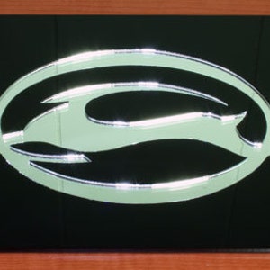 May include: Black license plate frame with a silver Chevrolet logo. The logo is a stylized bowtie with a silver finish.