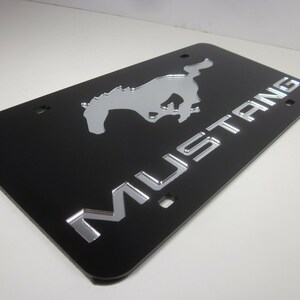 Puede incluir: Marco de matr&iacute;cula negro con un logotipo de Mustang plateado y la palabra "MUSTANG" en letras plateadas.