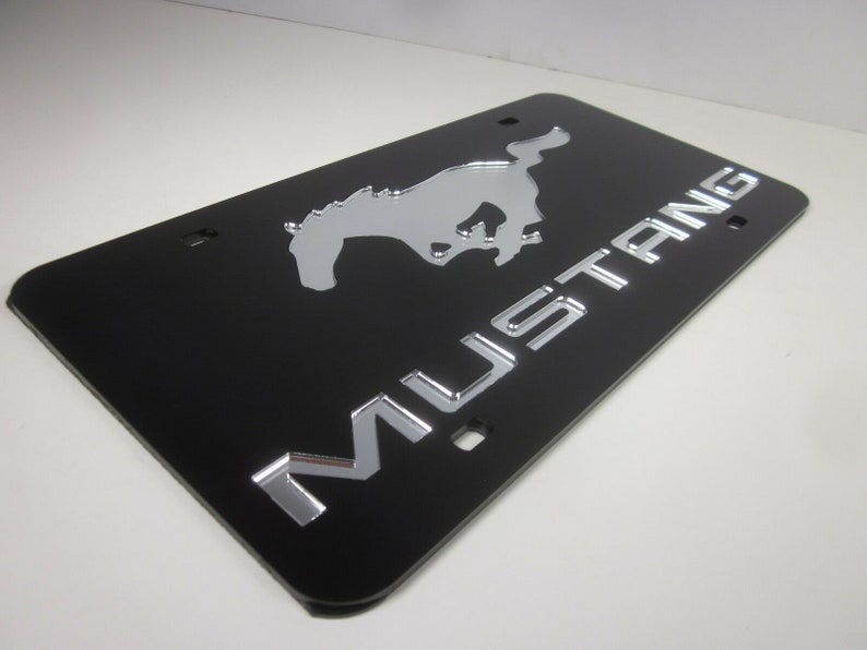 Puede incluir: Marco de matr&iacute;cula negro con un logotipo de Mustang plateado y la palabra "MUSTANG" en letras plateadas.