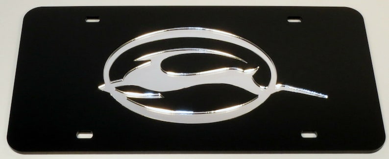 May include: Black license plate with a silver Chevrolet bowtie logo. The logo is a stylized silhouette of a bowtie with a silver finish.