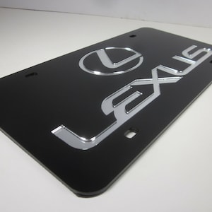 May include: Black license plate frame with a silver Lexus logo and the word "Lexus" in silver lettering.