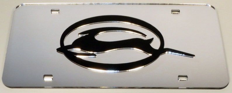 May include: A silver chrome license plate frame with a raised, black Chevrolet bowtie logo. The logo features a stylized running animal in a circle.