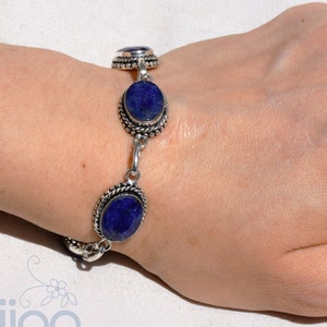 Puede incluir: Un brazalete de plata con tres piedras azules ovaladas. El brazalete está en la muñeca de una persona.