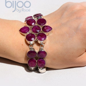 Op de afbeelding: Een zilveren armband met grote, ovaal geslepen, dieprode edelstenen. De armband heeft een bloemachtig ontwerp aan de bovenkant en een dubbele streng aan de onderkant. Het merk "bijoo by Rooxi" is zichtbaar.
